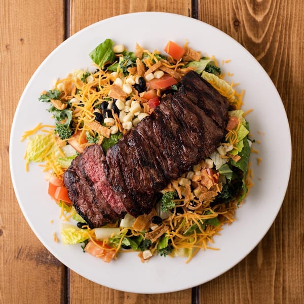 Honeybear Cafe's steak salad with corn, black beans, cheese, and tortilla strips on a white plate.