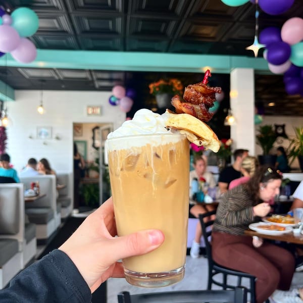 Hand holding a Honeybear Cafe iced coffee topped with whipped cream, bacon, and a pancake.