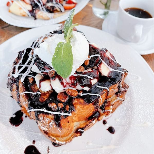 French toast topped with chocolate sauce, whipped cream, bananas, nuts, and a mint leaf.